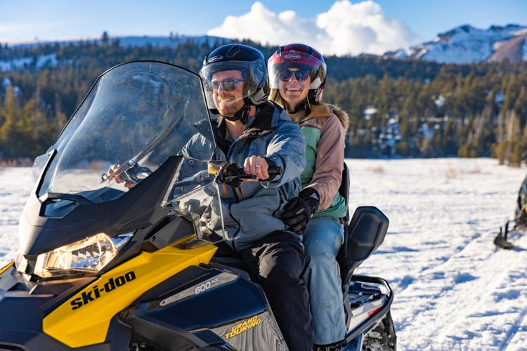 Two snowmobilers ride a snowy mountain trail